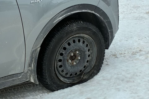 A silver car with a flat front tire parked on a snowy surface.